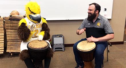 Gilbert the Eagle playing a drum with a CSI Professor
