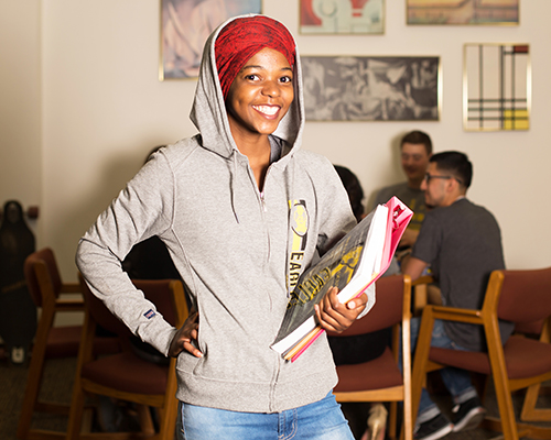 A student posing for the camera holding books and a binder