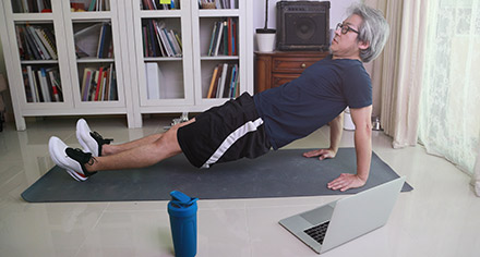 man doing a plank exercise next to his laptop
