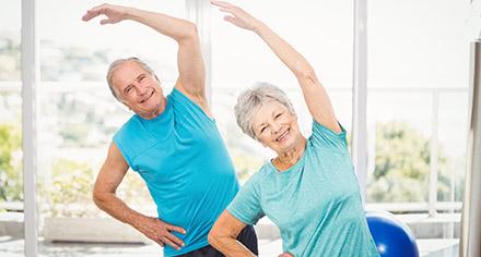 grey-haired couple doing yoga stretches in a classroom