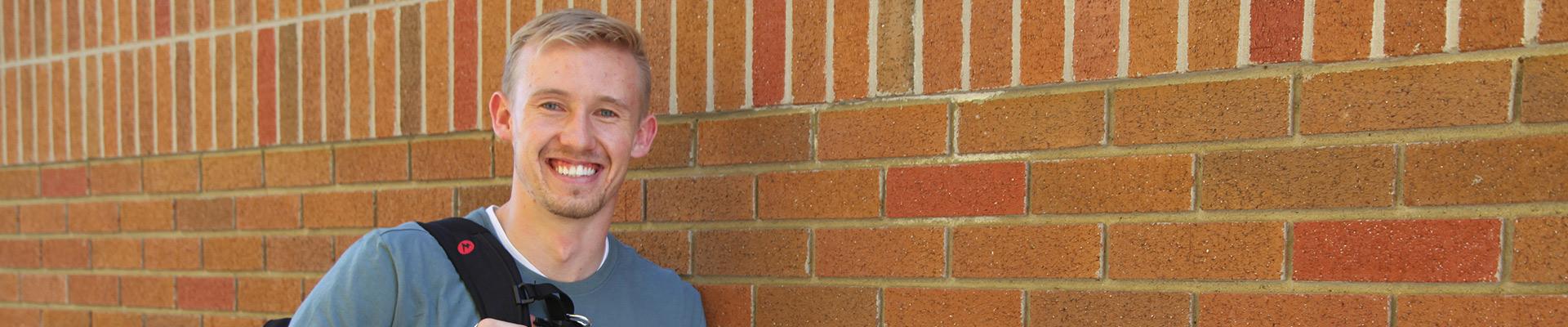 College Student standing in front of a brick wall.