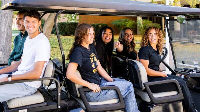 Students riding a golf cart across campus