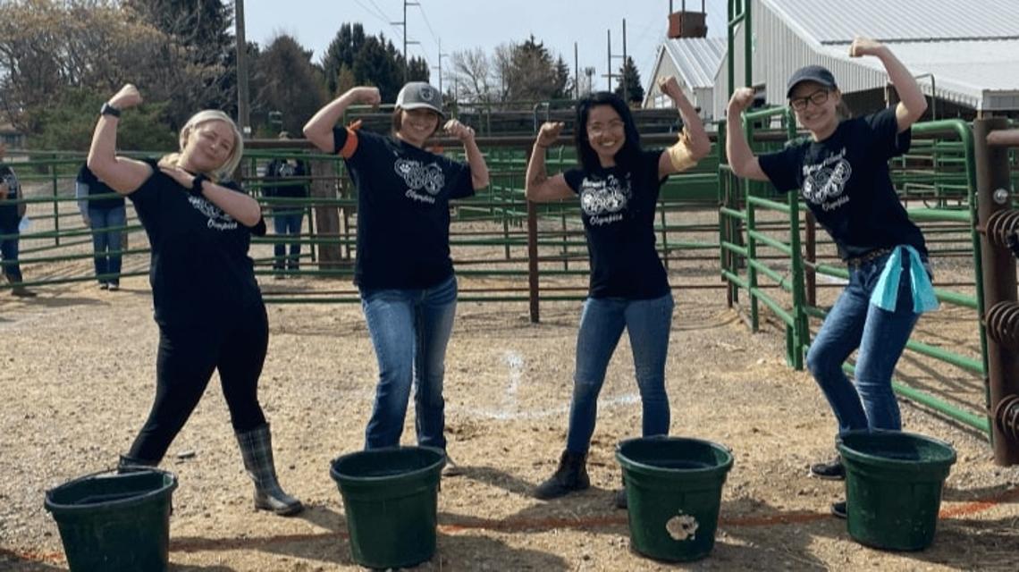 Four contestants posed in an arena with black feed buckets in front of them
