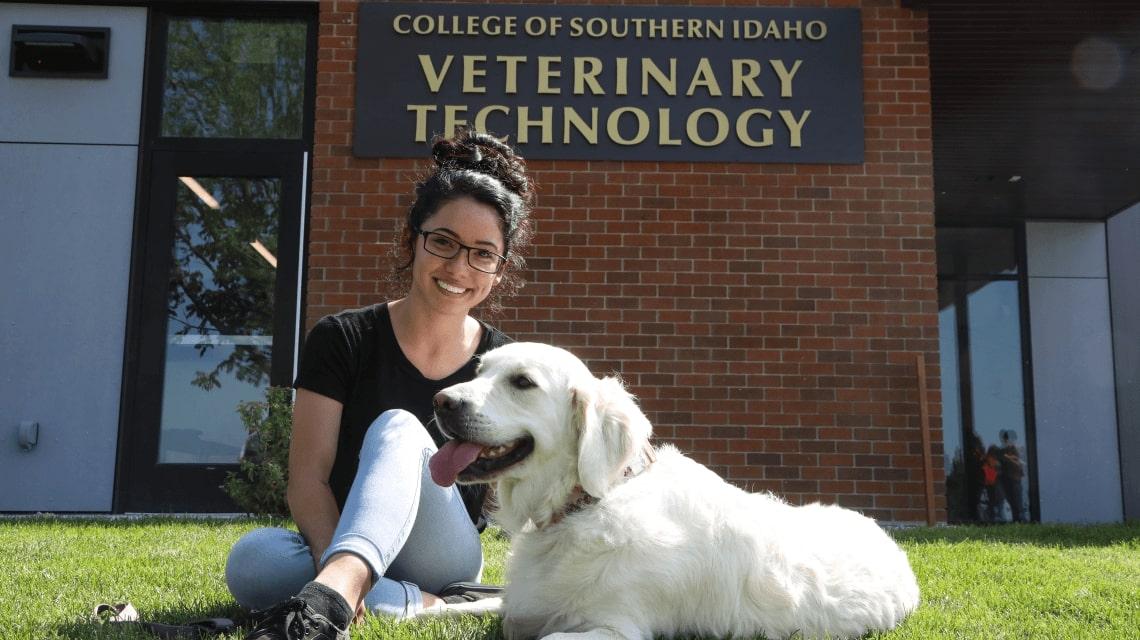 A student sits in the grass with a dog