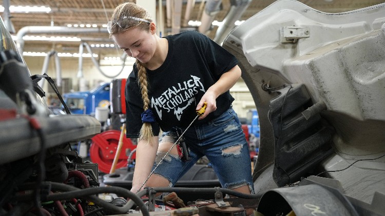 A woman pulling a dipstick out of an 18 wheelers engine