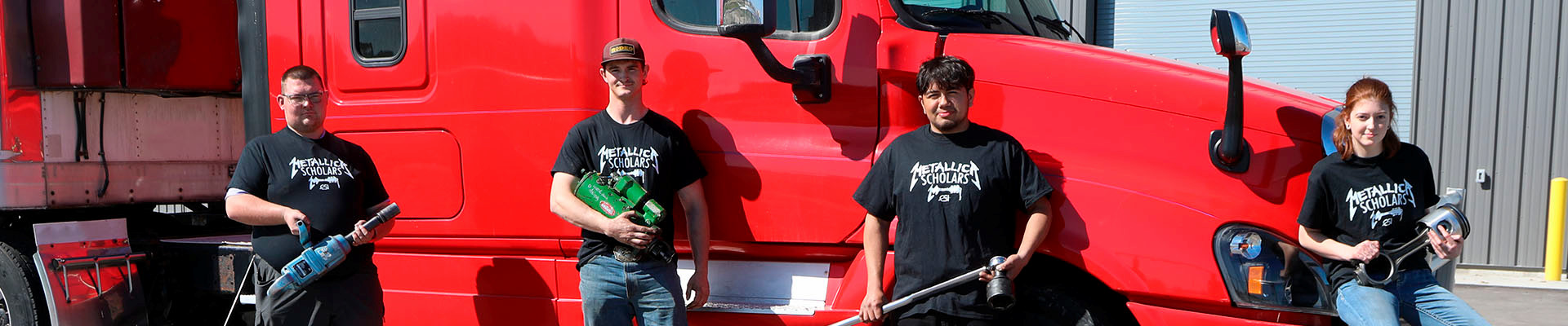 Four Diesel Tech students holding tools in front of an 18 wheeler 