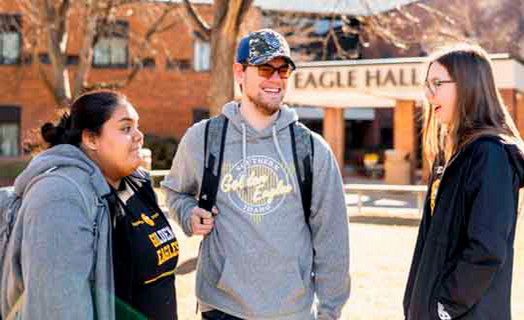 2 female students and one male student standing in front of eagle hall building wearing hoodies