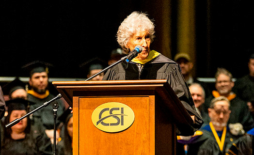 Maxine Bell wearing graduation regalia at a CSI podium