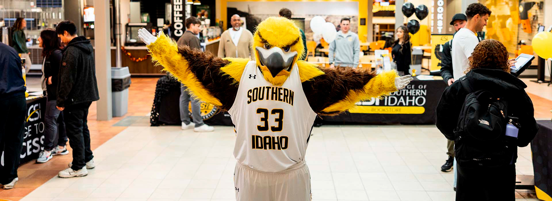 Gilbert the golden eagle standing in a room full of tables and several people milling around. 