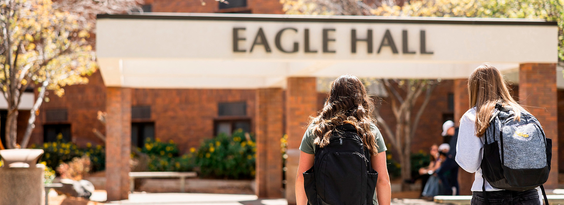 2 female students with their backs to the camera,walking towards the CSI dormitory with the words Eagle Hall on the building. 