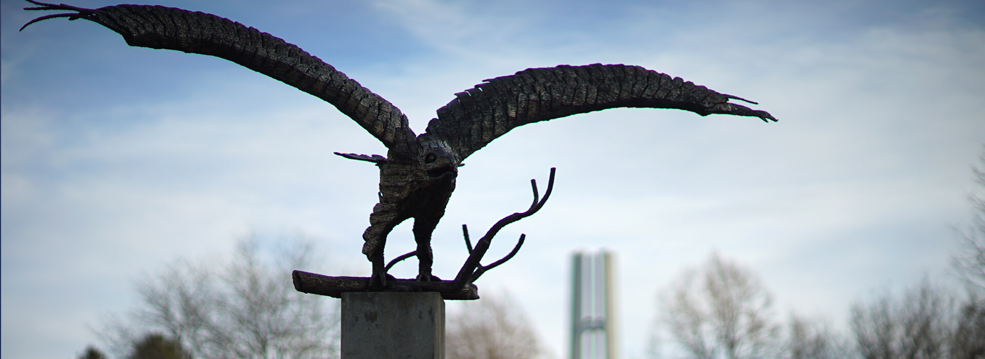 Golden Eagle Statue with gray sky and leafless trees in the background with the bell tower peaking out in the back