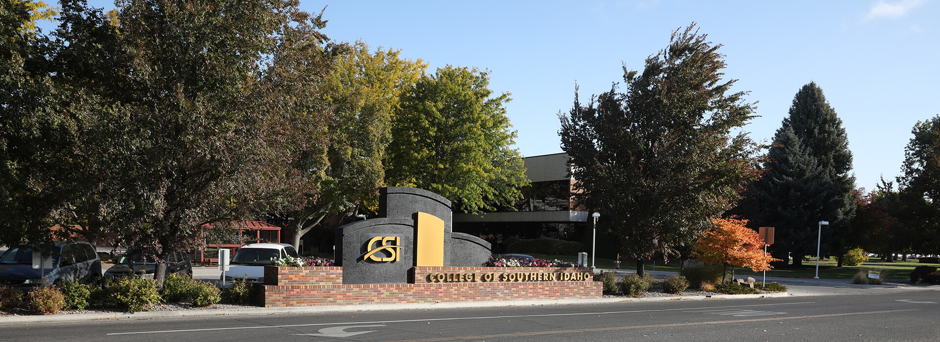 CSI main entrance sign with road going in front of it. Trees in the background, and the Taylor building behind it.