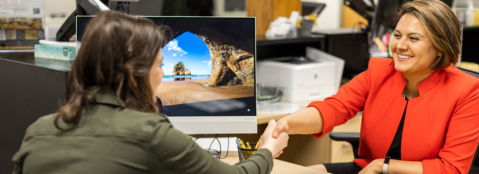 Monze wearing red shaking hands with a female student that is wearing green in Eagle Central