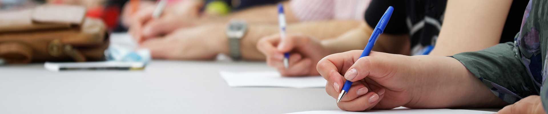 photo of people with pens in hand sitting at table discussing something