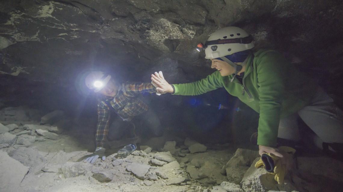Two students high five inside a cramped cave