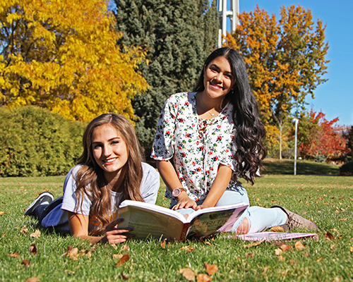 Two students sitting on the grass, reading, on the CSI campus