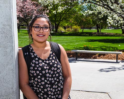 A student standing next to the CSI tower with the grass and trees in the background