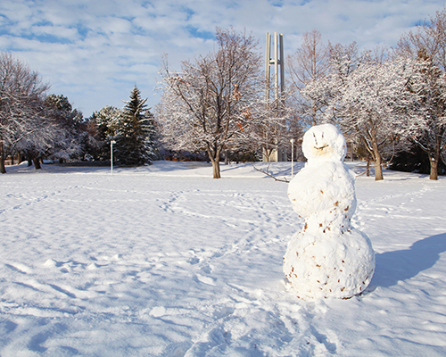 snowman on a sunny day, CSI campus in background with brown leaveless trees