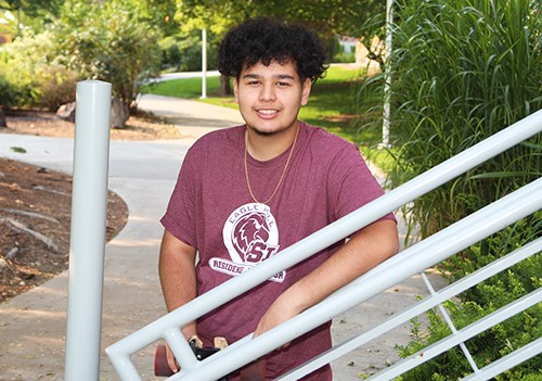 A smiling student standing outside, leaning on a gaurdrail