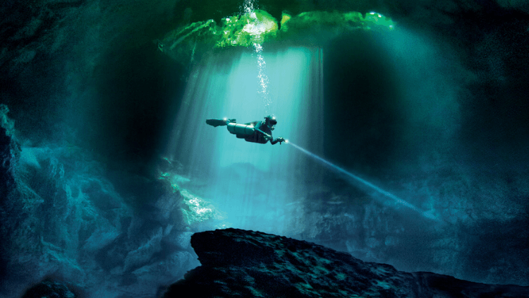 A cave diver in the center of a pool with a flashlight