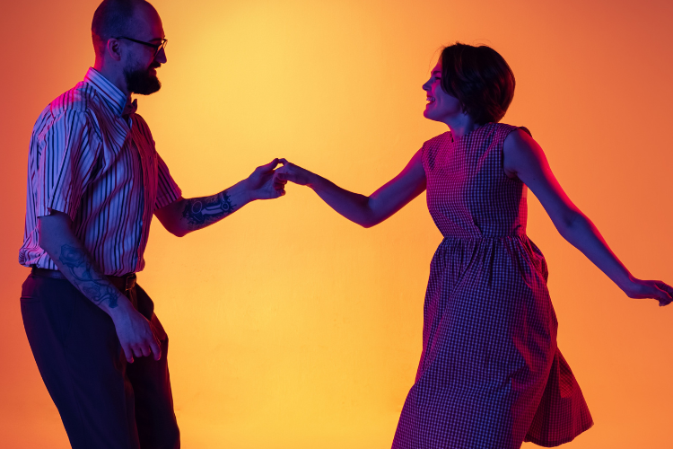 A man and a woman dancing together in a low light environment, with a orange background